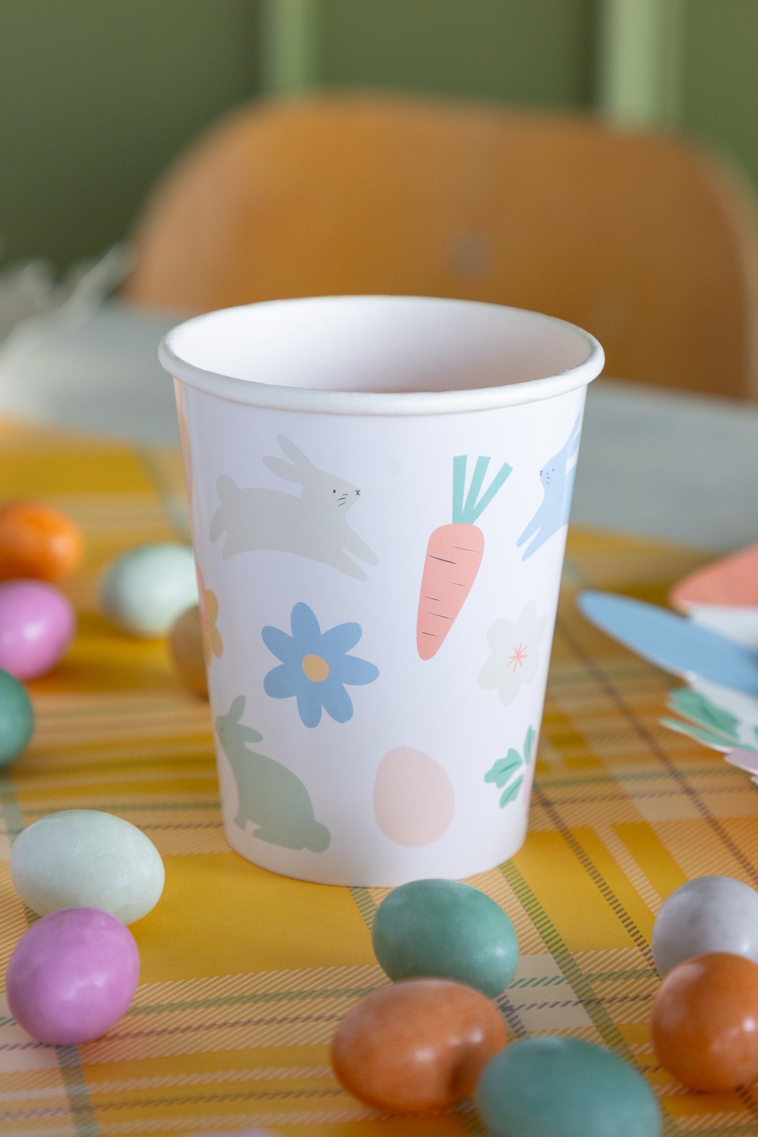 Paper cup with Easter icons on a table with colorful eggs.