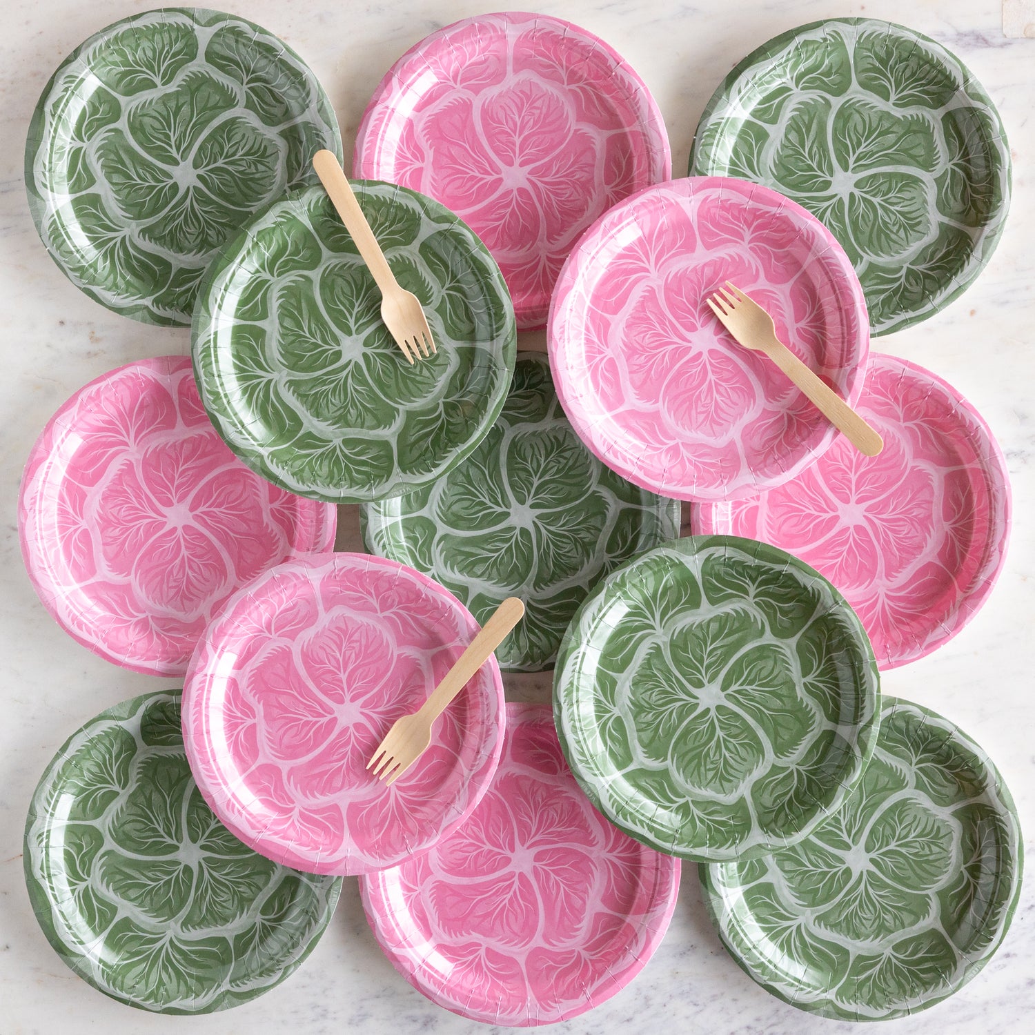 Set of pink and green cabbage patterned paper plates with wooden forks on a white surface.