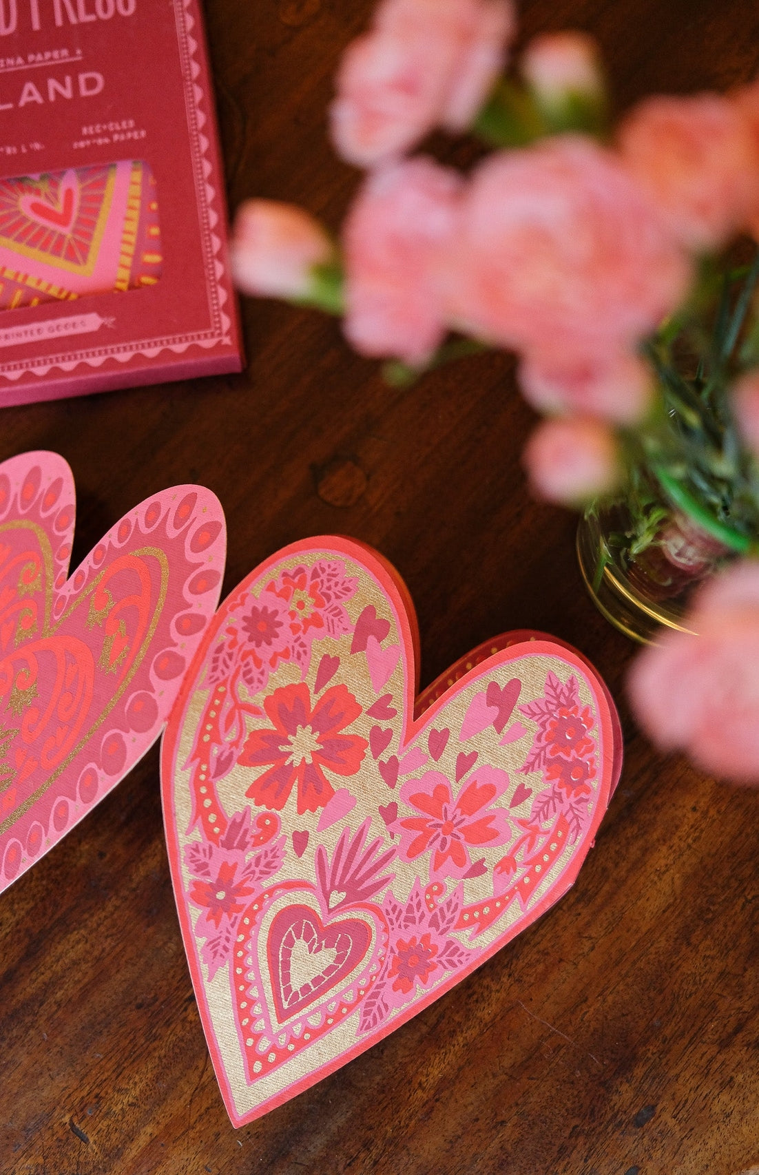 Decorative pink heart-shaped garland on a wooden surface with flowers in the background.