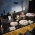 Halloween-themed table setting with decorative plates, cups, and a black tablecloth.