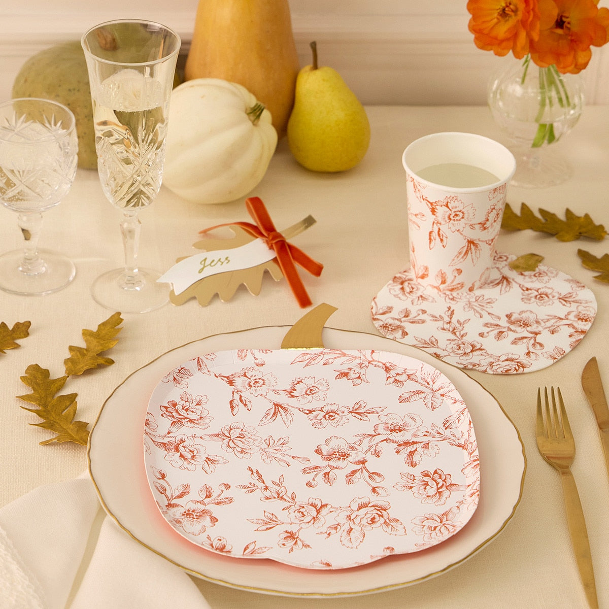 Dining table setting with floral-patterned plates, cups, and cutlery on a neutral background.