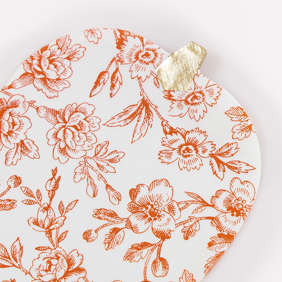 Pumpkin shaped plate with orange floral pattern and gold leaf on a white background.