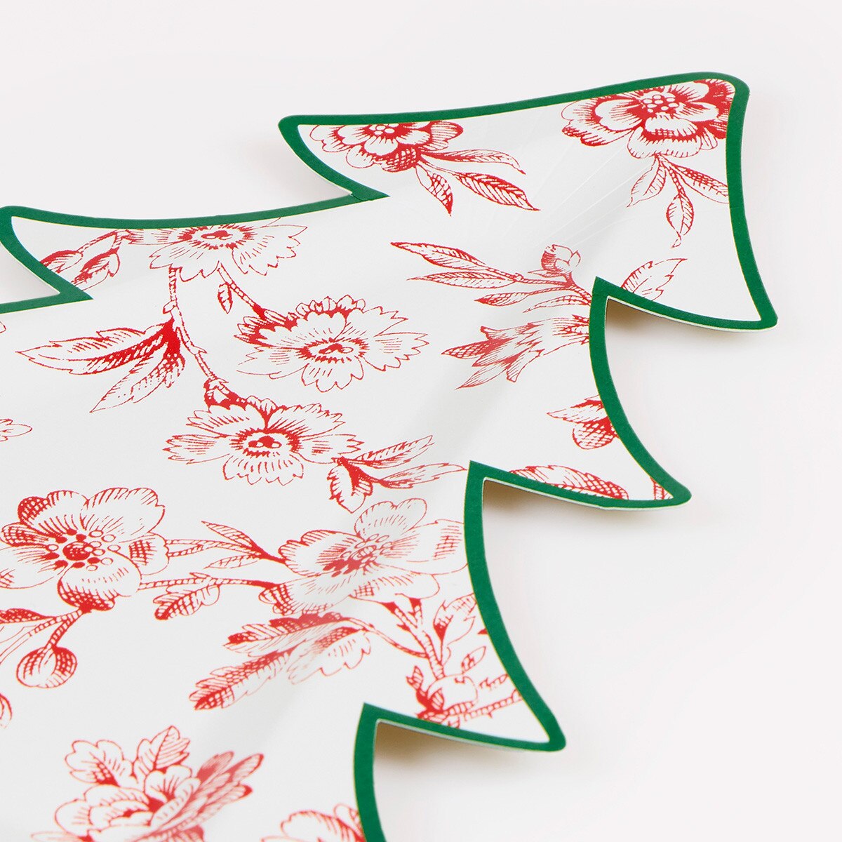 A close-up of a white paper plate shaped like a Christmas tree with a red floral toile pattern and a green edge.