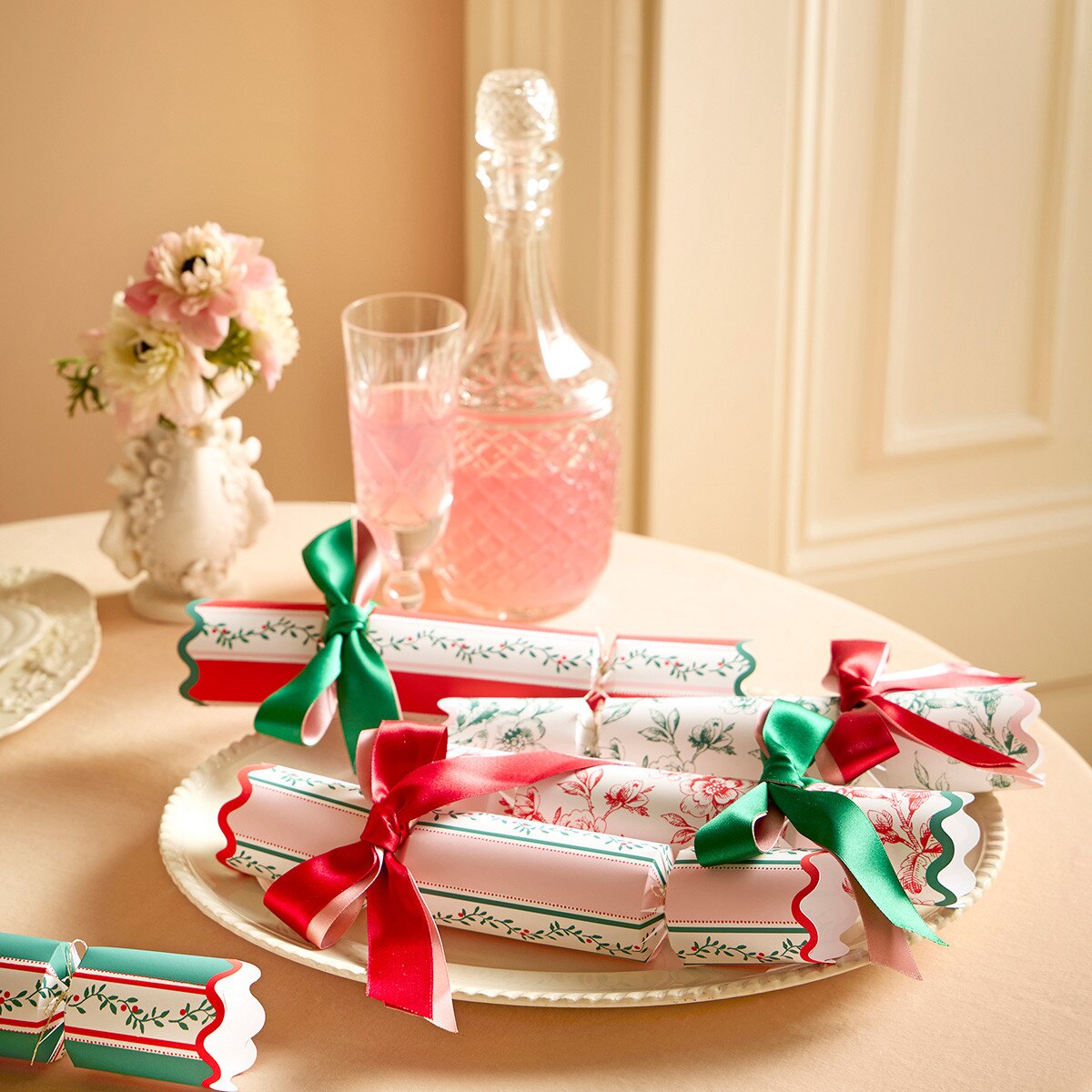 Decorative crackers with red and green ribbons on a table with a bottle and glass.