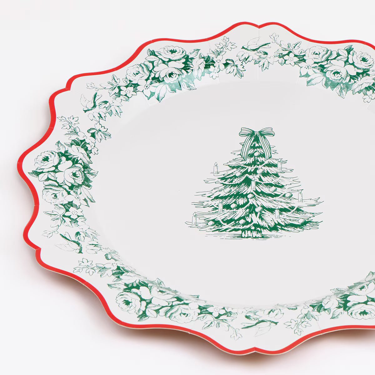 A white paper plate with a scalloped edge, featuring a green floral border and a green mistletoe tree illustration in the center, with a thin red rim.