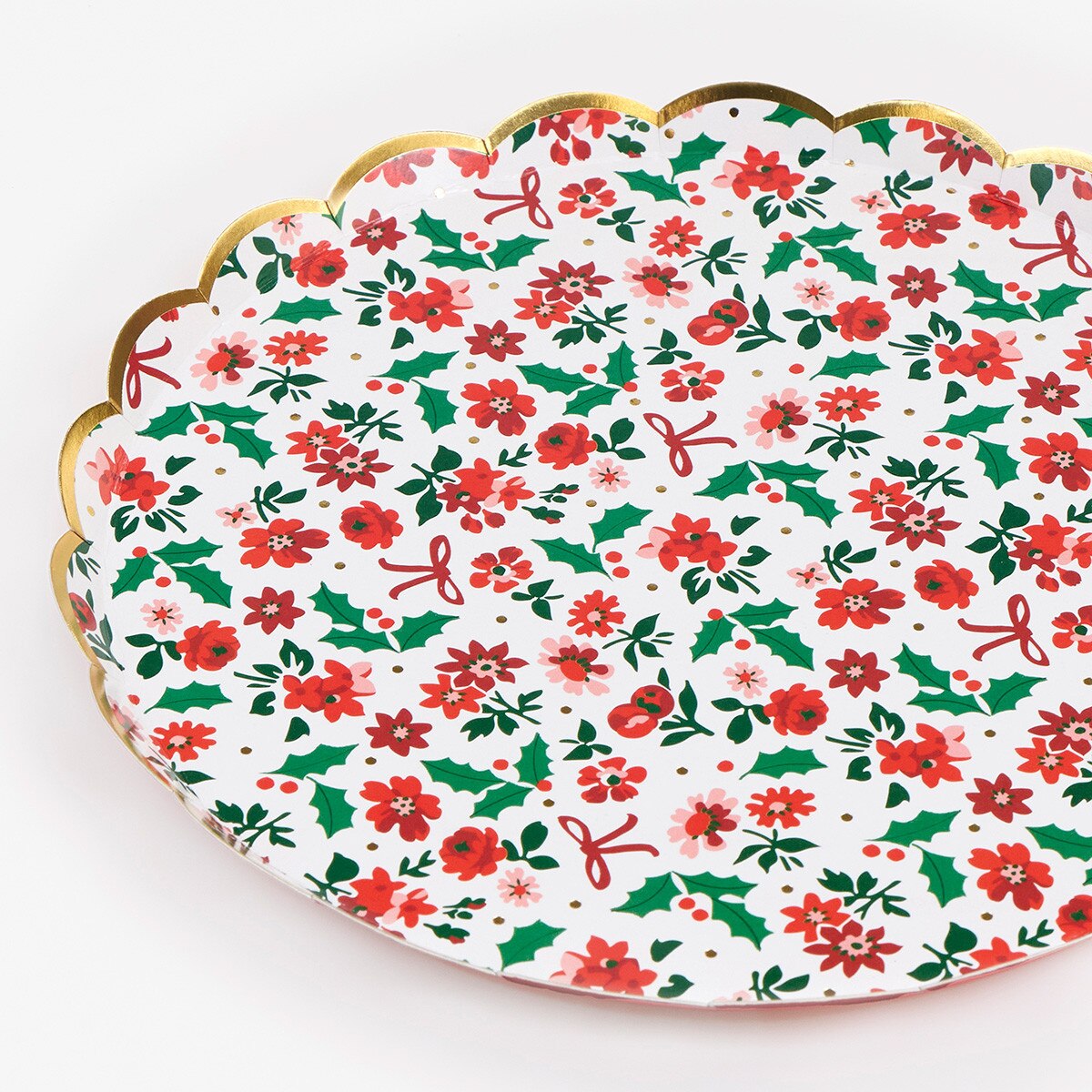 A scalloped oval serving platter with a festive Christmas pattern of red poinsettias, green holly leaves, and red bows on a white background, finished with a gold metallic rim.
