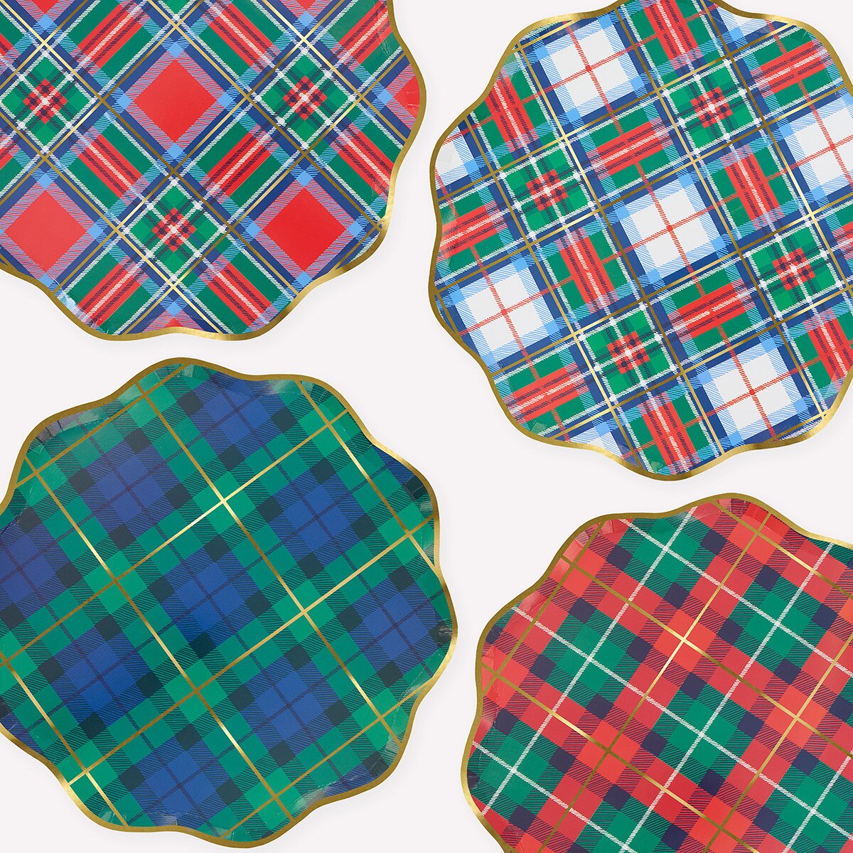 Four scalloped-edge tartan plaid paper plates with gold trim, arranged in a 2x2 grid on a white background. Each coaster features a different holiday tartan pattern: red and green, blue and green, blue and green, and red and green.