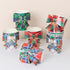 A set of 8 paper cups decorated with colorful tartan plaid bands and large matching paper bows, arranged on a light neutral background.