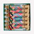 A boxed set of dachshund-shaped paper cracker ornaments with colorful plaid patterns and ribbon accents, arranged inside a green gift box on a light gray background.