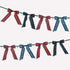 A festive garland banner with alternating tartan plaid ribbon bows in red, navy, and blue-green plaid patterns, strung along a dark green cord with small gold bells.