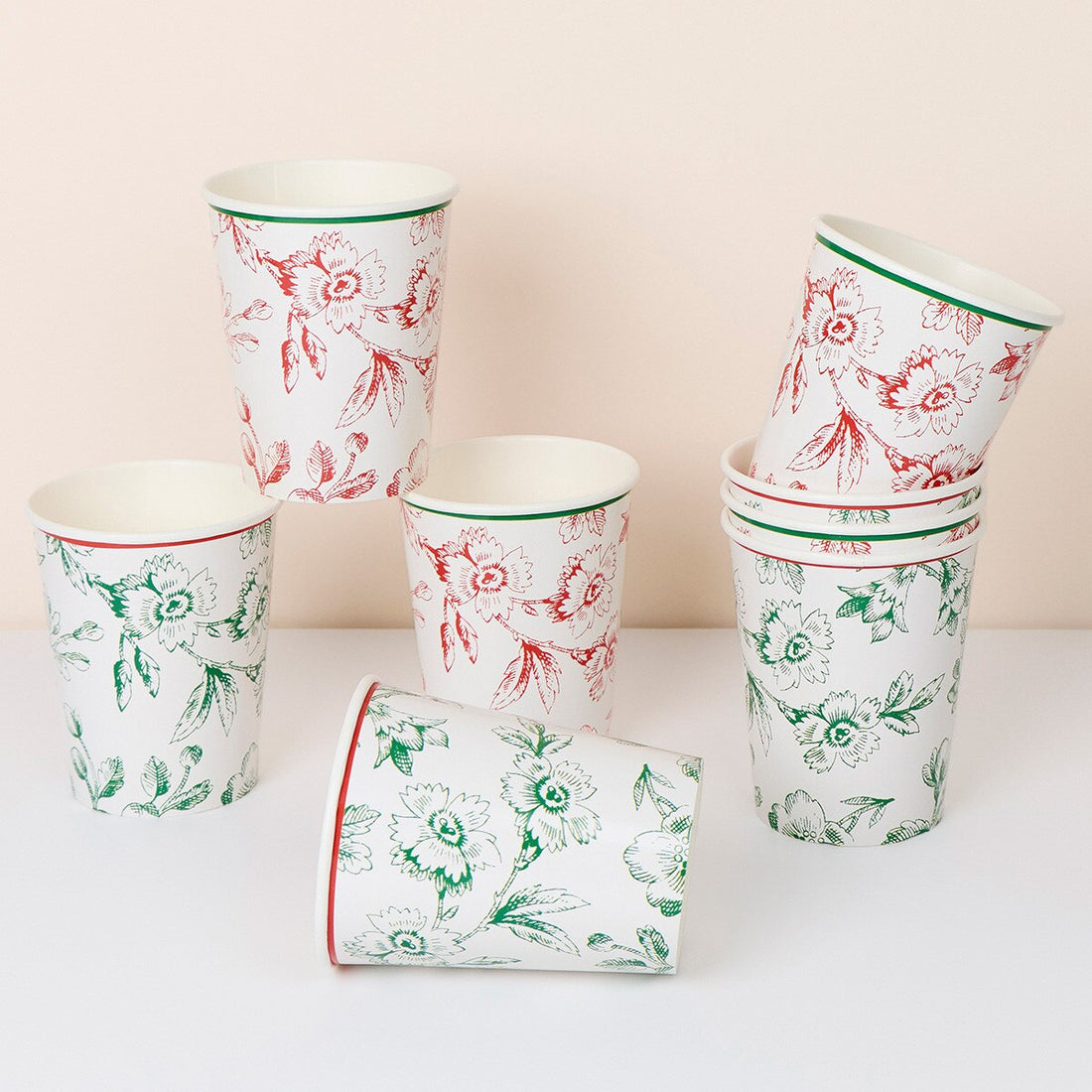 A set of white paper cups with floral patterns in red and green, arranged on a white surface against a light beige background.