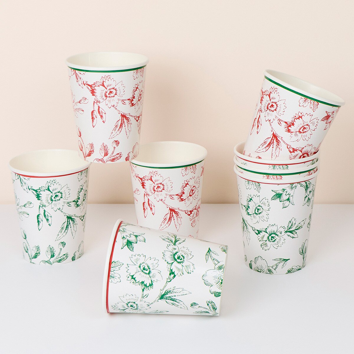 A set of white paper cups with floral patterns in red and green, arranged on a white surface against a light beige background.