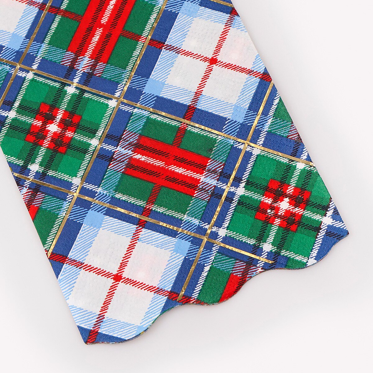 A close-up of a folded plaid fabric, likely a napkin or decorative paper, featuring a festive Christmas tartan pattern with green, blue, red, and white stripes.