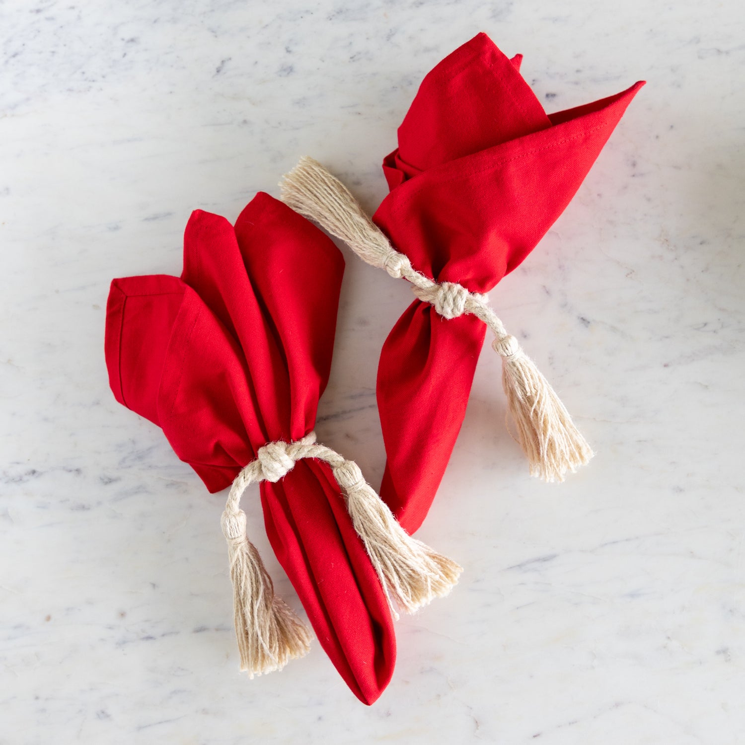 Two red napkins with beige tassels on a marble surface.