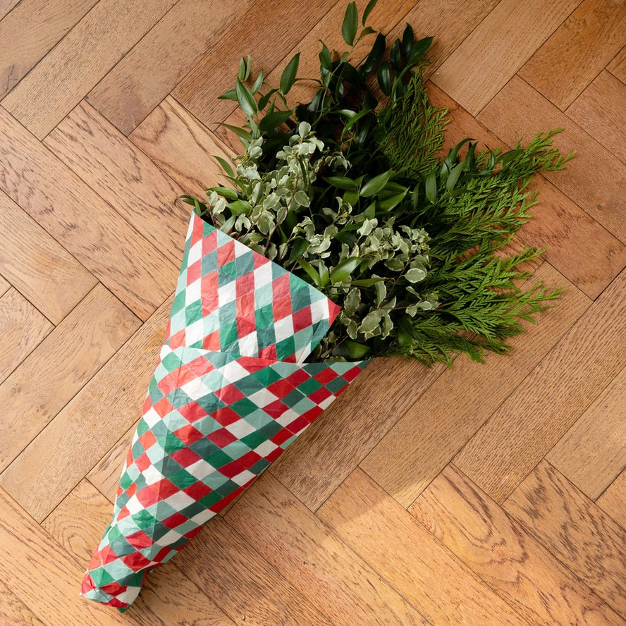 Bouquet of greenery wrapped in a red and green checkered paper on a wooden floor.