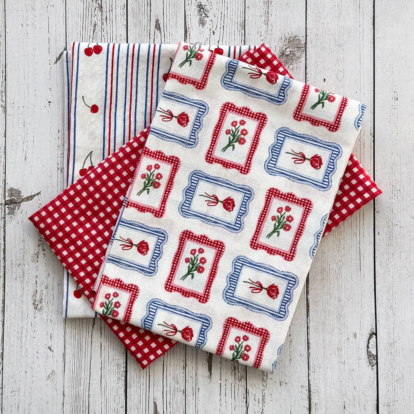 Collection of fabric tea towels with red, white, and blue patterns on a wooden surface.