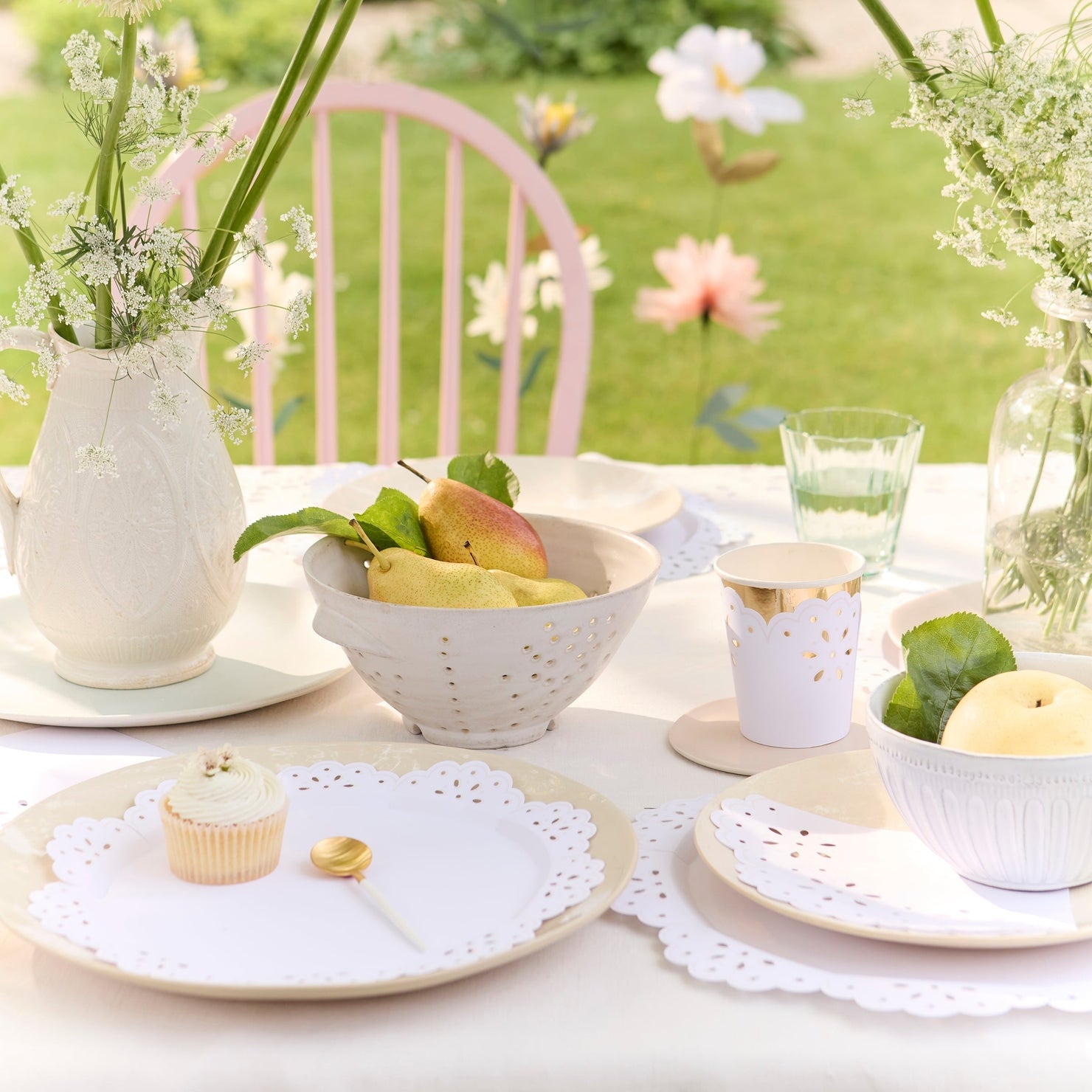 Outdoor table setting with flowers, fruit, and pastries on a white tablecloth.