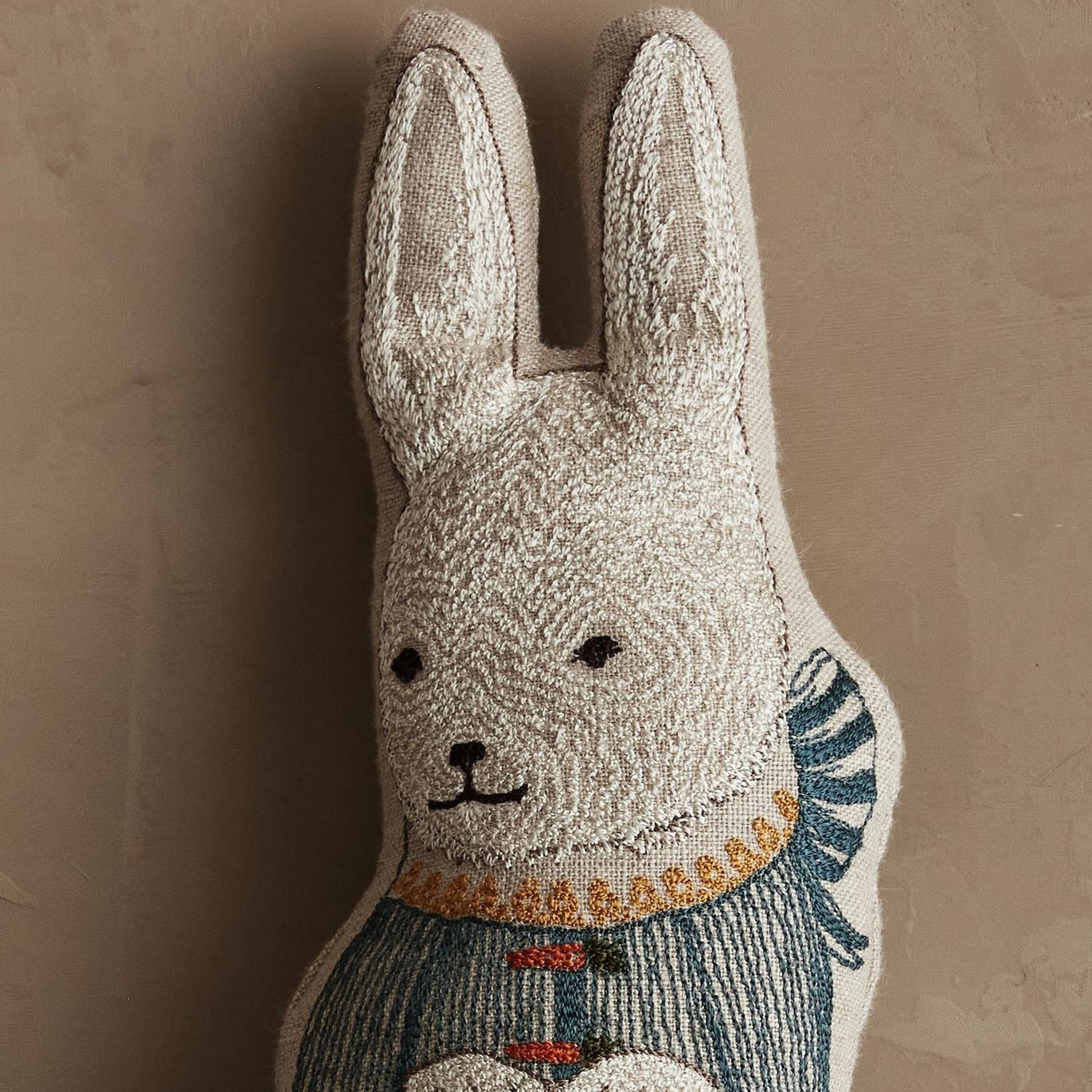 Decorative rabbit plush toy with embroidered details on a beige background.