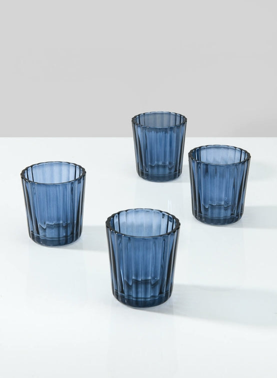 Four blue glass tumblers on a white surface with a light gray background.