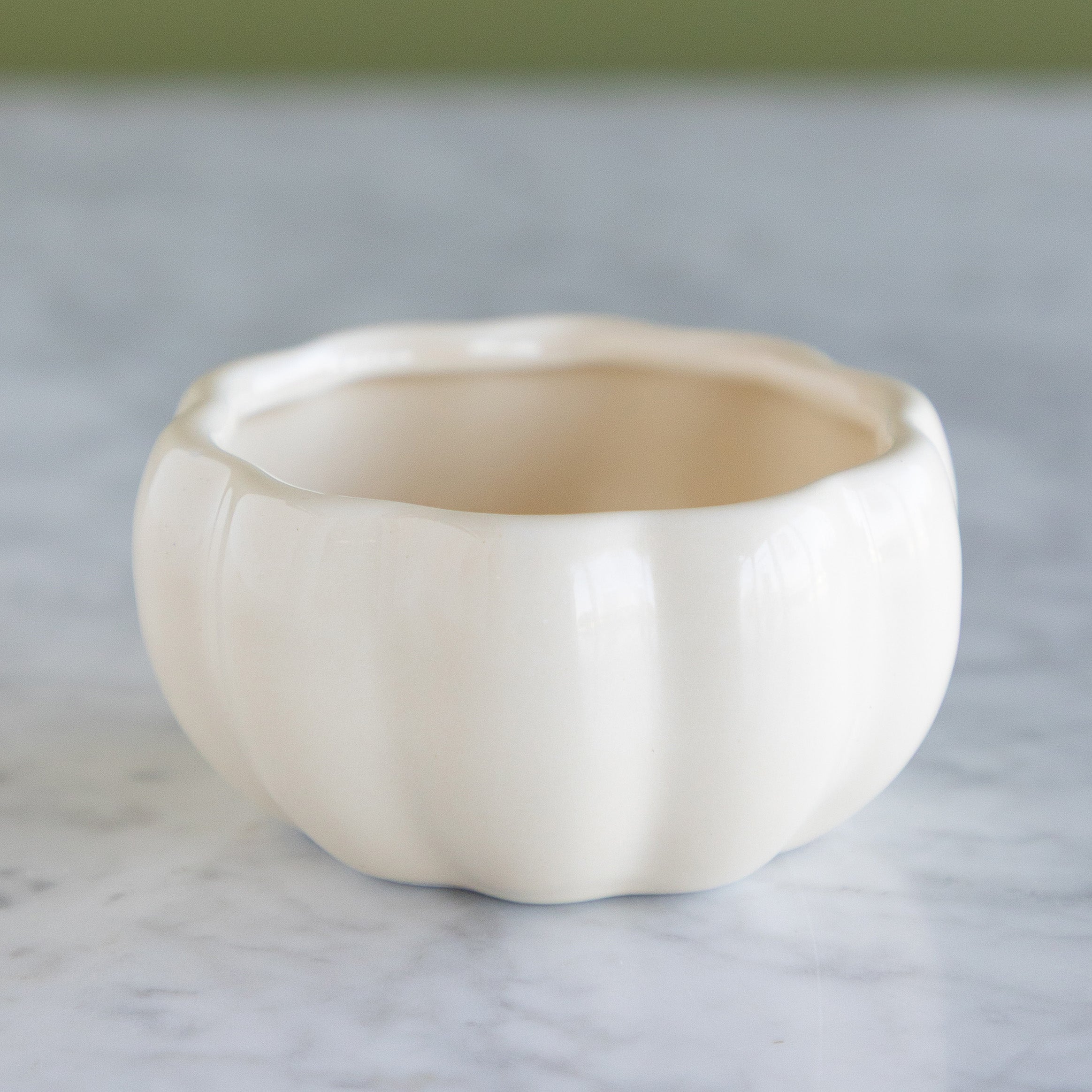 An off-white ceramic bowl with a ribbed pumpkin-like design, sitting on a light gray marble surface.