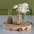 Two gold rabbit sculptures on a wooden stand with a vase of white flowers in the background.