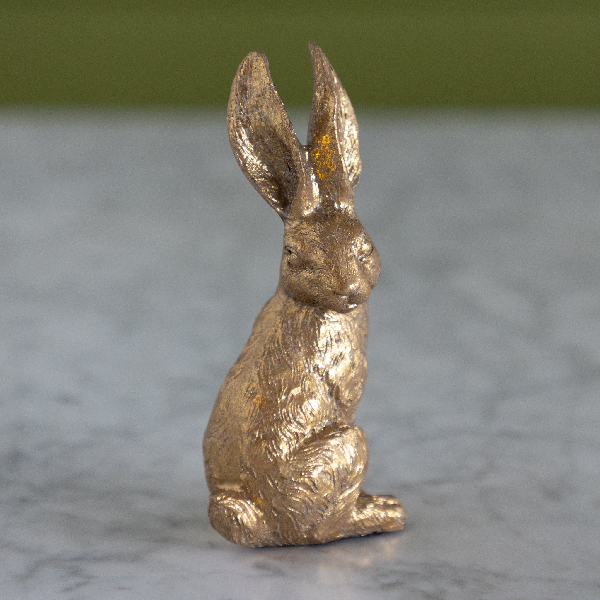 Bronze rabbit figurine on a marble surface with a blurred green background.