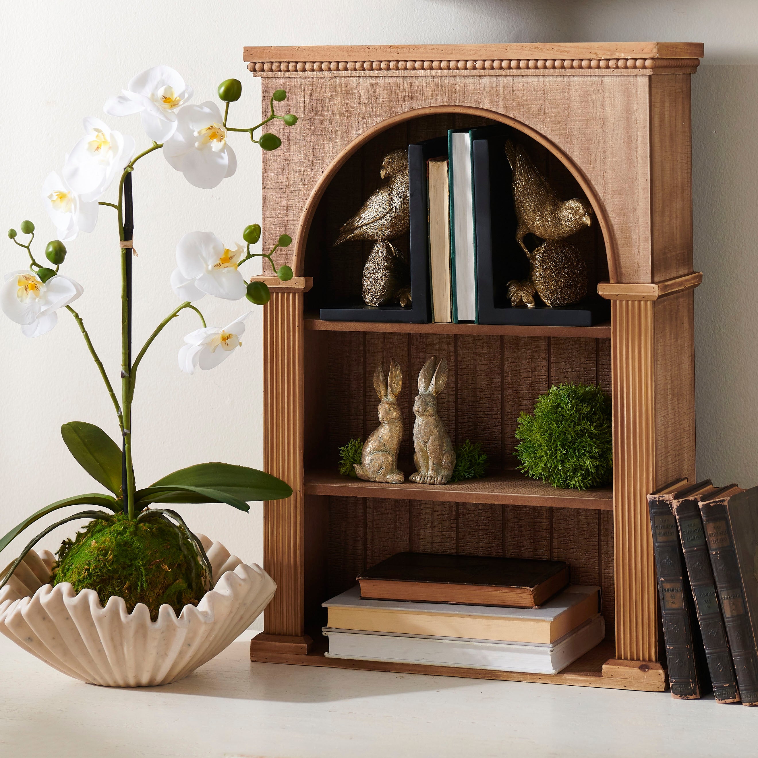 Wooden bookshelf with decorative items including Gold Leaf Rabbits, books and figurines, next to a potted plant.