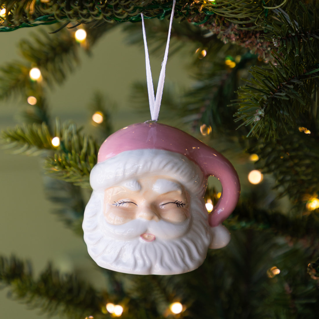 Pink Santa Ornament featuring a jolly santa with his eyes closed and a pink hat, hanging on a lit Christmas tree.