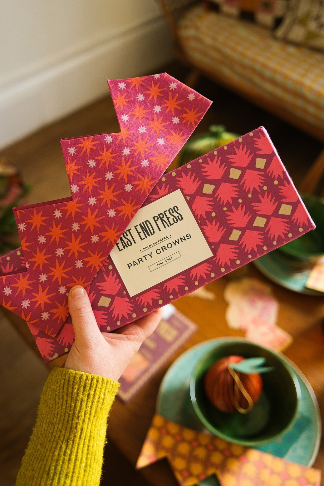 Person holding a box of East End Press party crowns with decorative patterns.