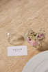 Decorative glass vases with flowers on a beige surface, name card &