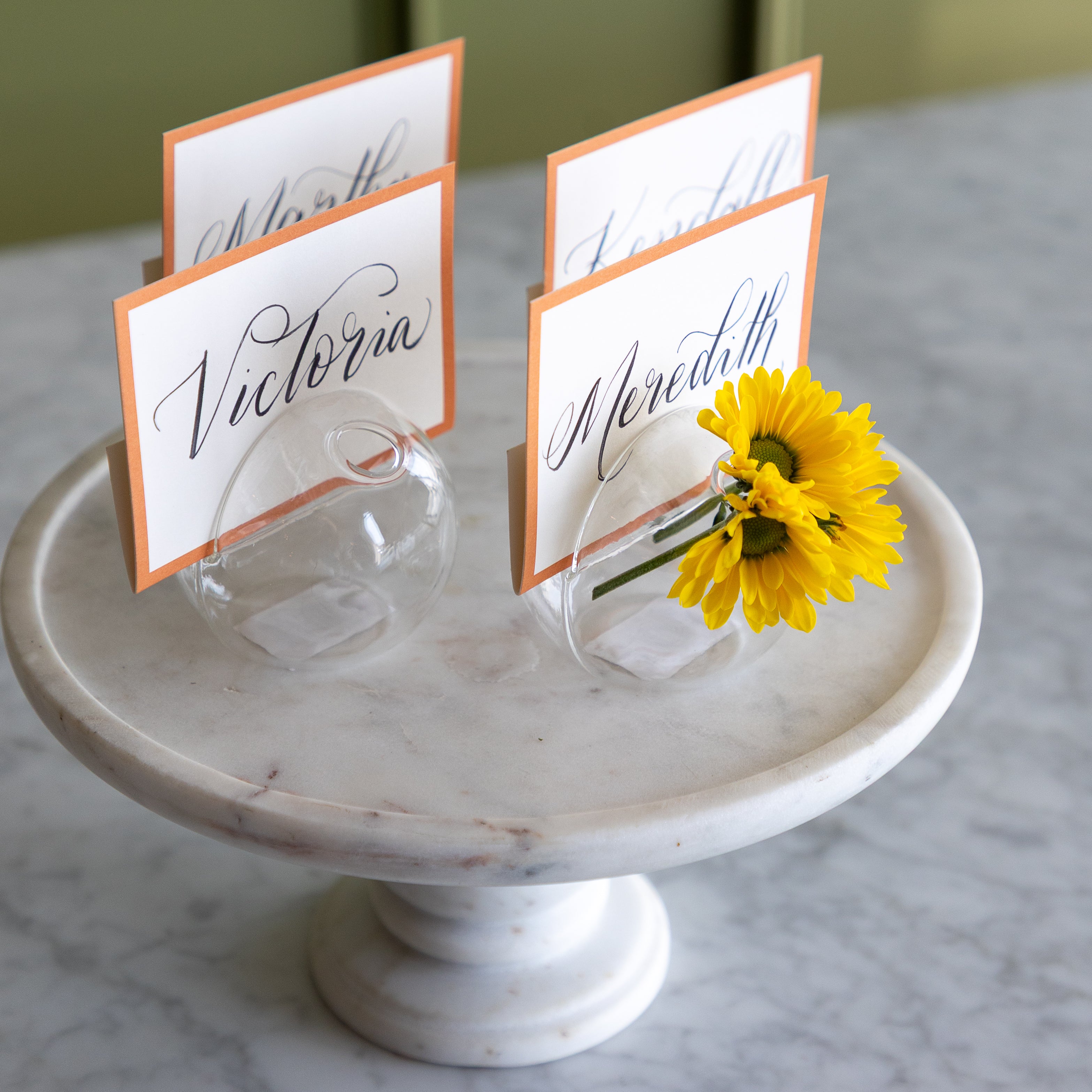 Table name cards on a marble stand with a yellow flower.