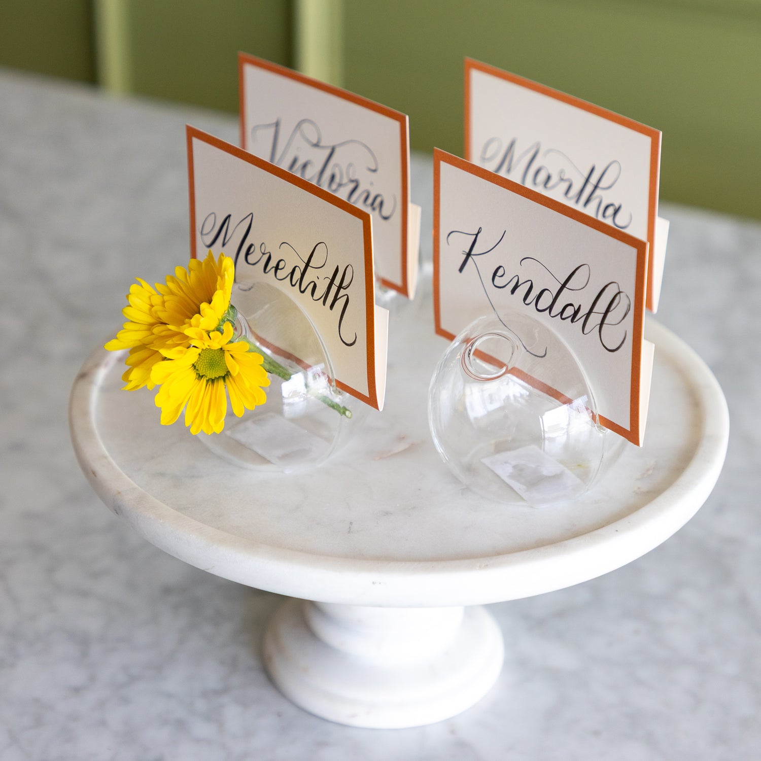 Table name cards on a white pedestal with a yellow flower.