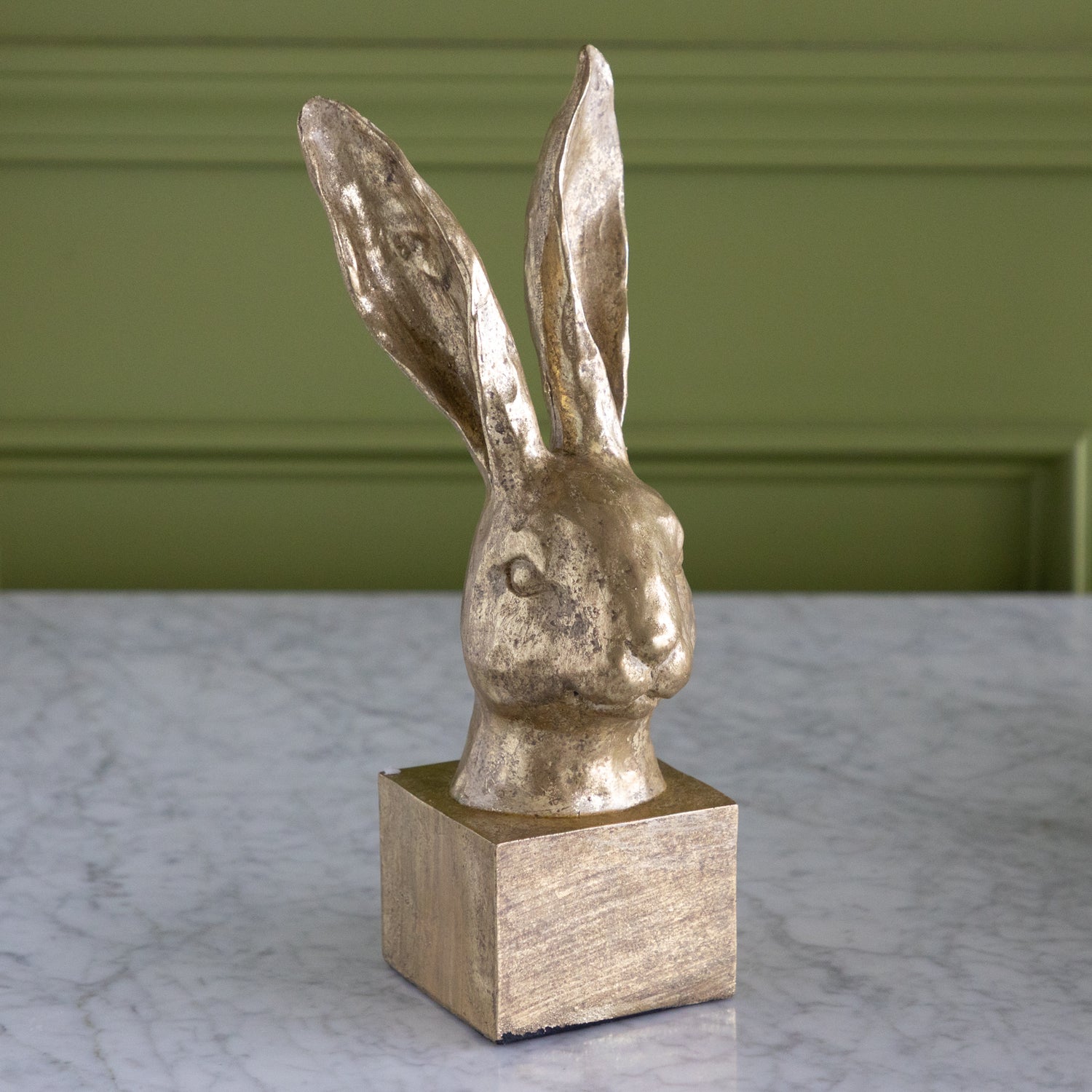 Decorative rabbit head sculpture on a square base against a green wall.