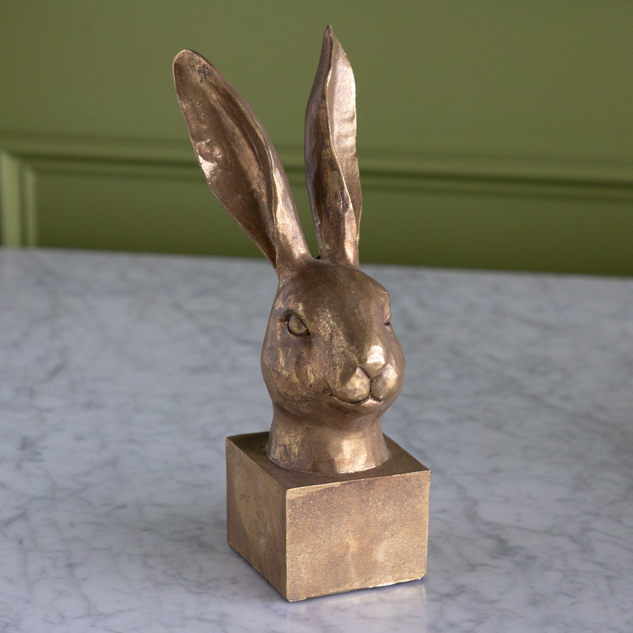 Bronze rabbit sculpture on a marble surface with a green wall background.