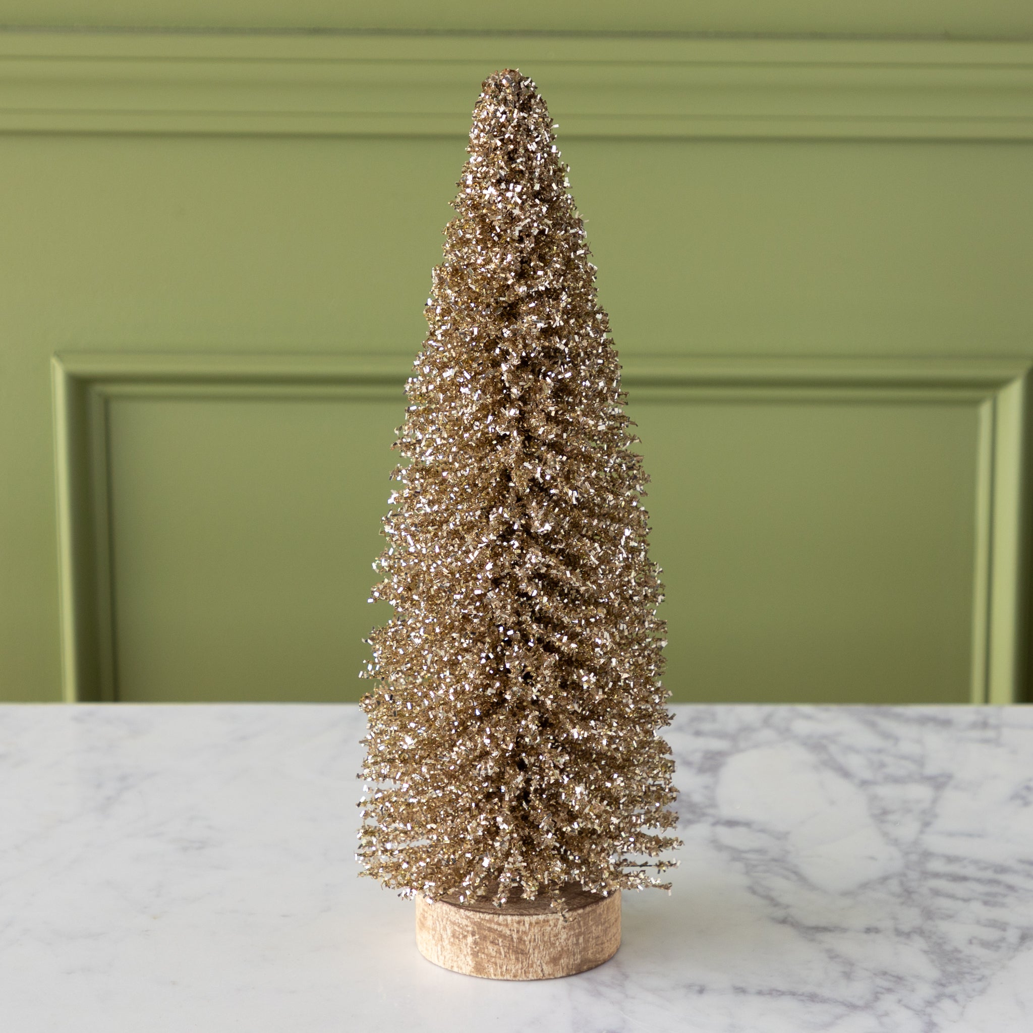 Gold glittery bottlebrush tree on a wooden base, on a marble surface.
