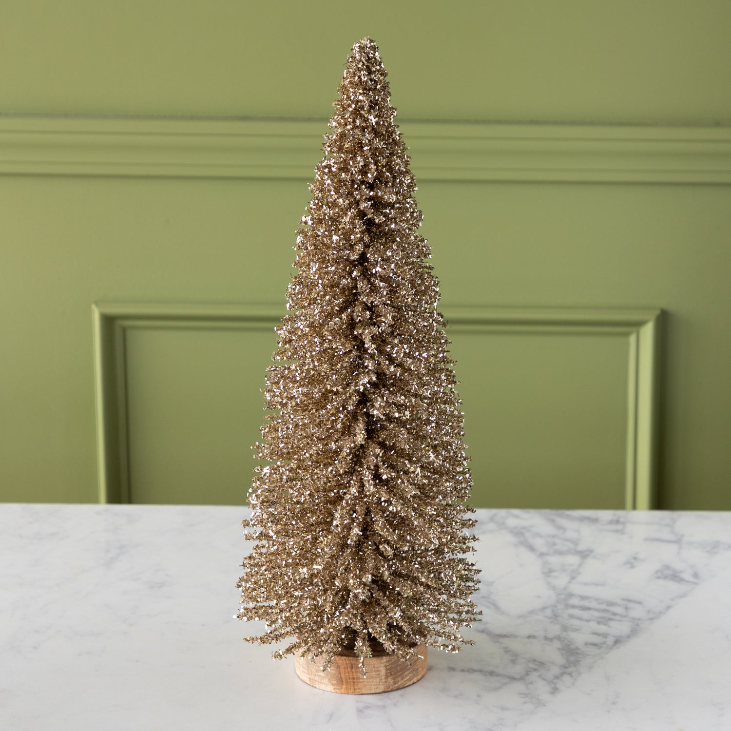 Gold glittery bottlebrush tree on a wooden base, on a marble surface.