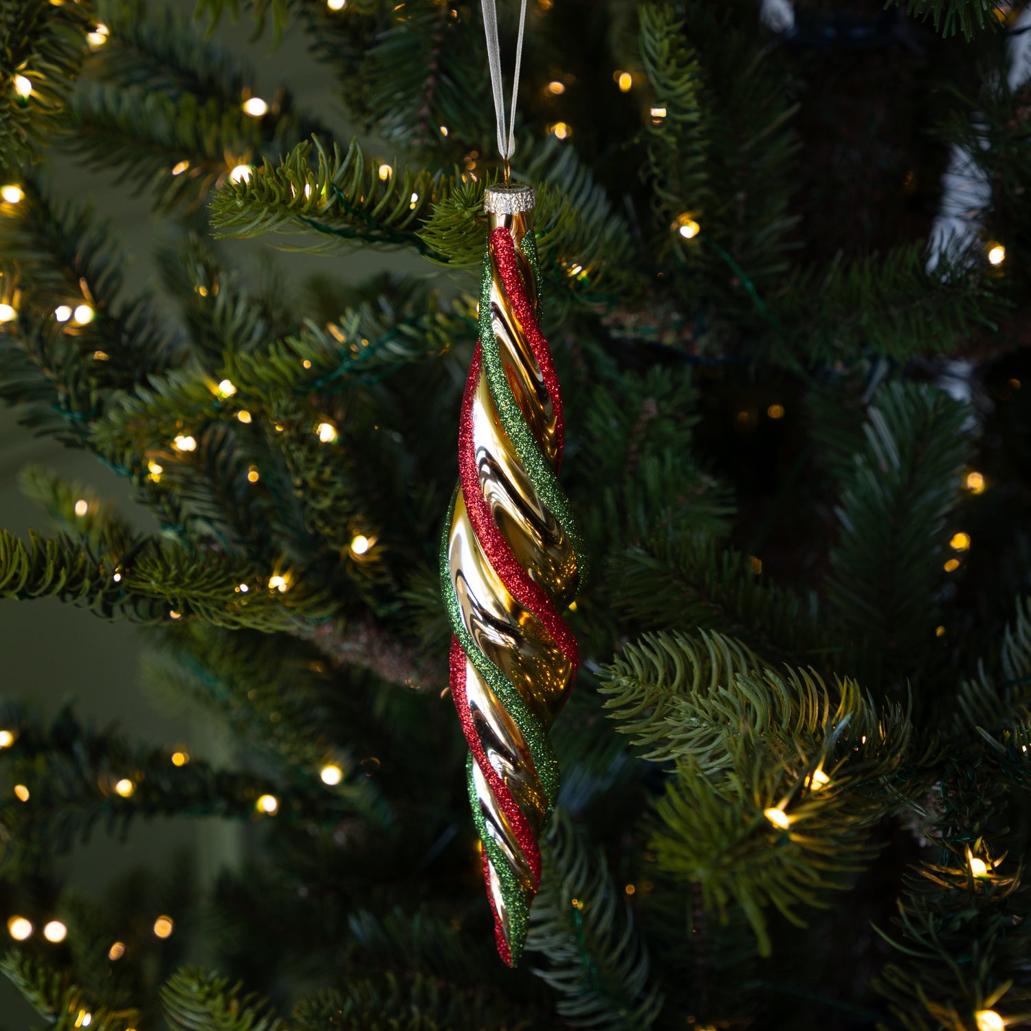 Red &amp; Gold Twirl Ornament with a gold base and glittery red and green swirls on a lit Christmas tree.