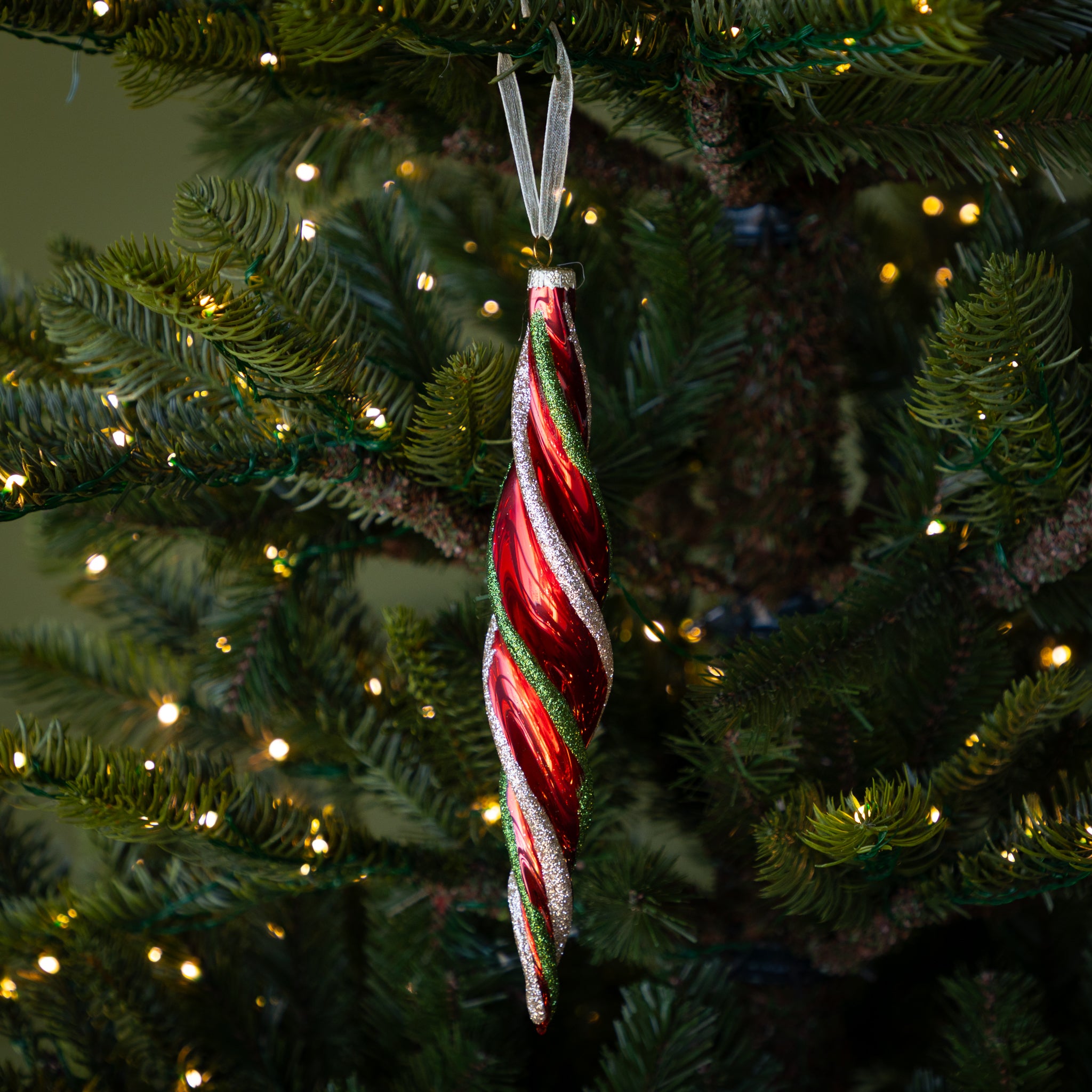 Red &amp; Gold Twirl Ornament with a red base and glittery red and green swirls on a lit Christmas tree.