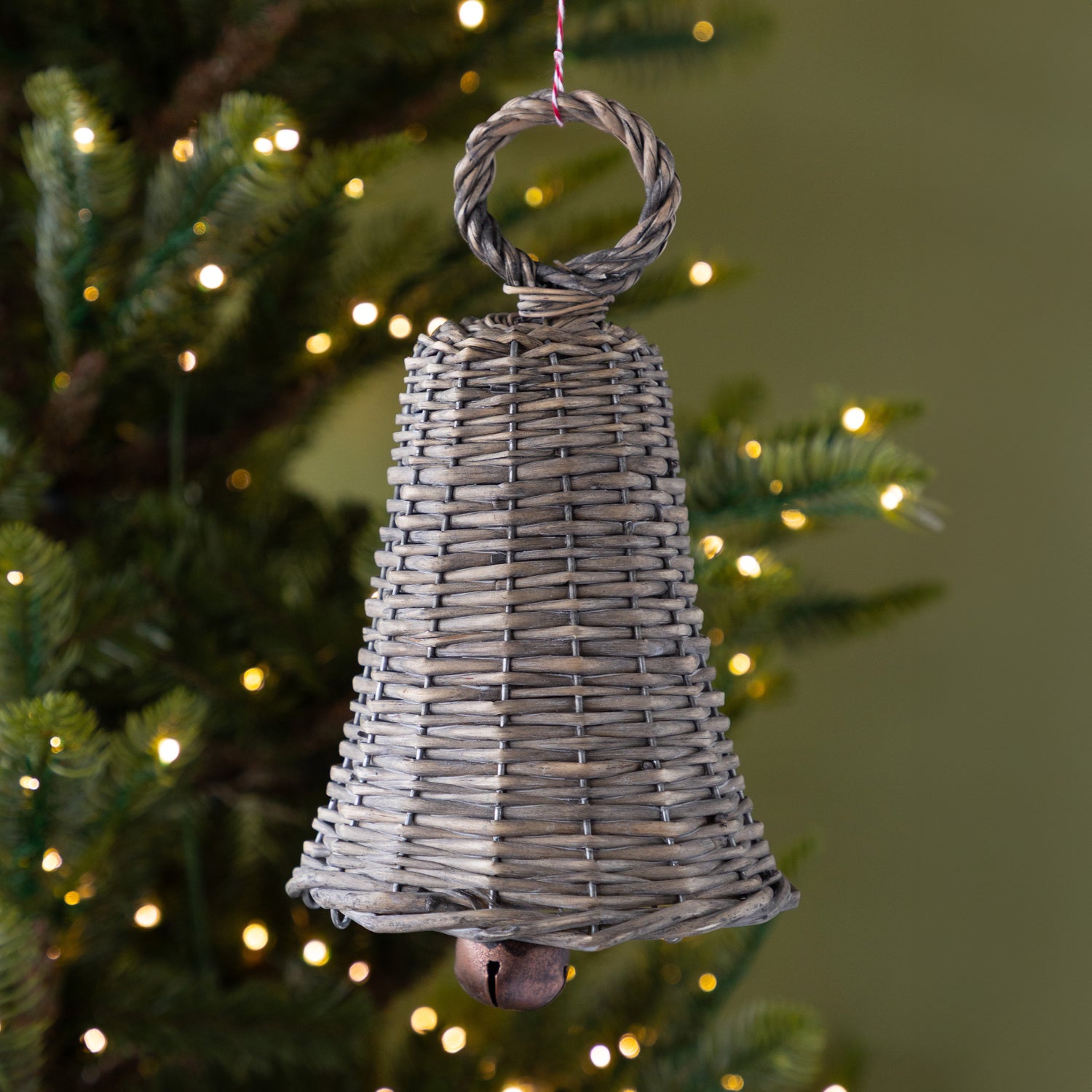 Wicker bell ornament hanging on a Christmas tree with lights in the background.