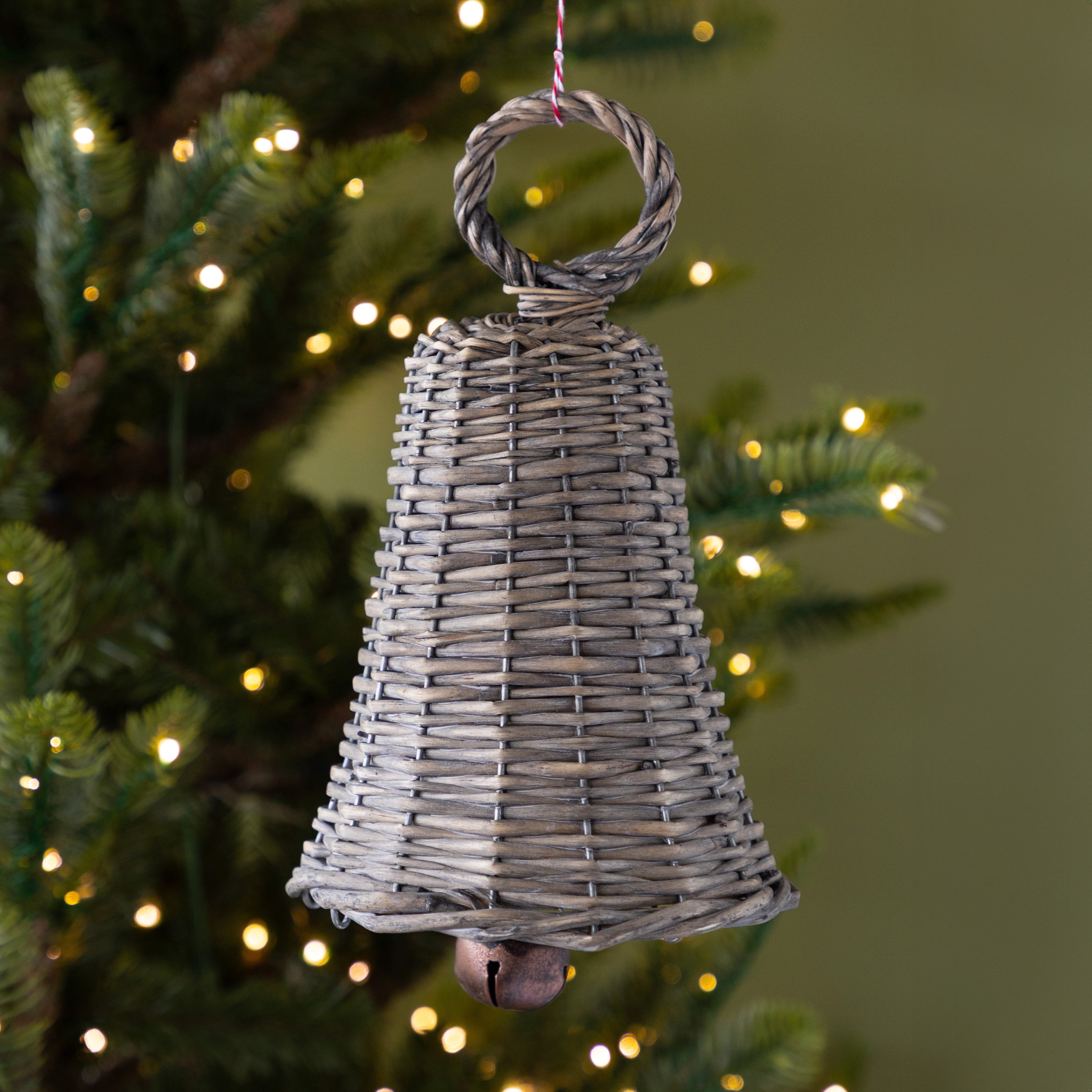Wicker bell ornament hanging on a Christmas tree with lights in the background.