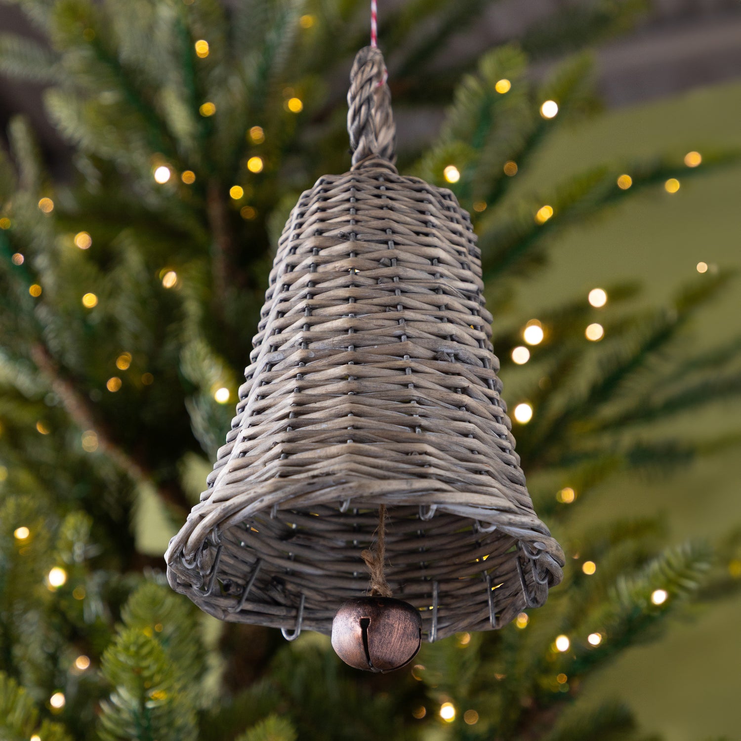 Wicker bell ornament hanging on a Christmas tree with lights in the background.