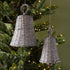 Two woven bell ornaments hanging on a decorated Christmas tree.