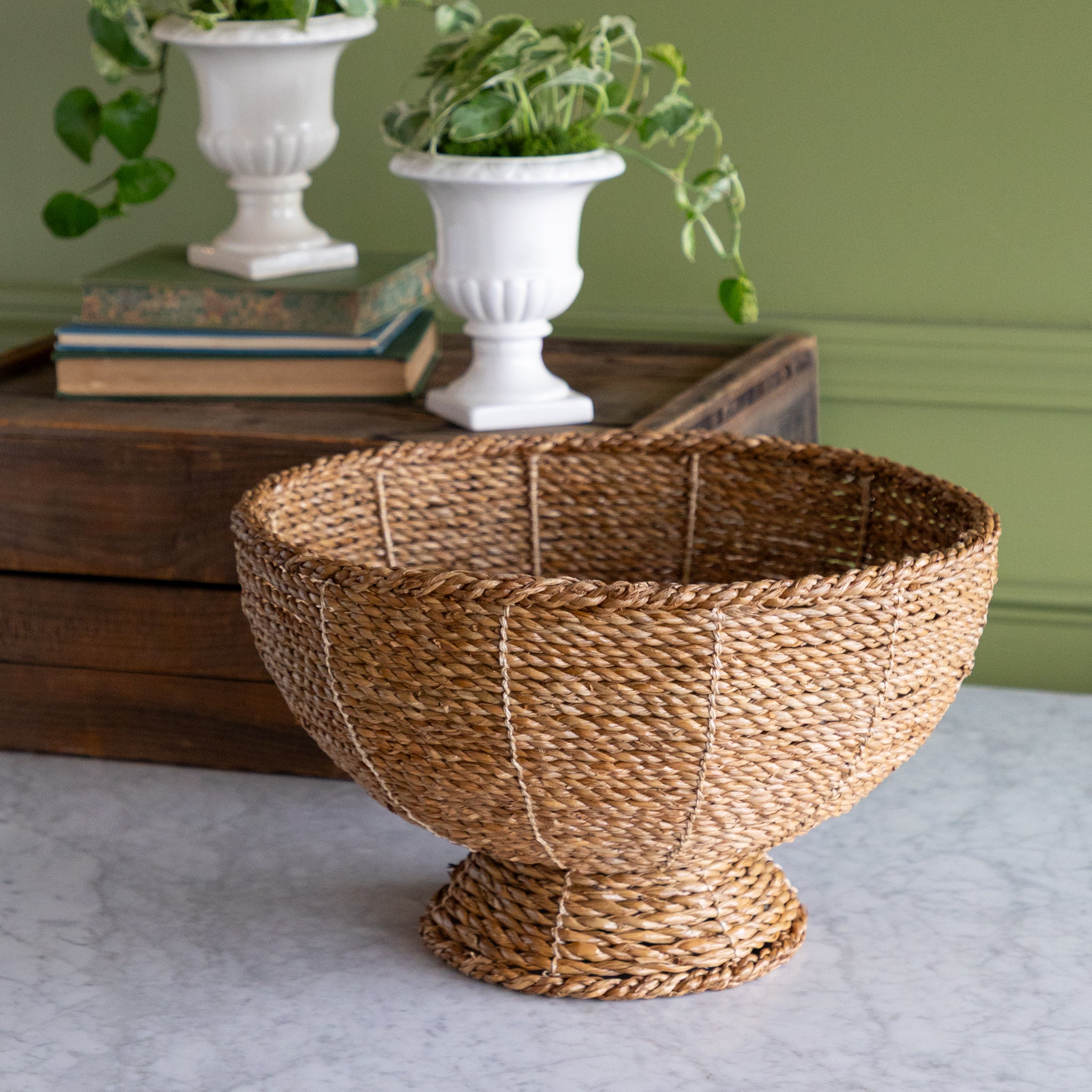 Natural Rope Weave Bowl on marble surface with a wooden box, books and a plant in the background.
