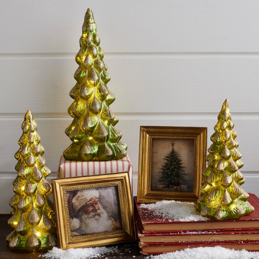Decorative lighted Christmas trees with a framed picture of Santa Claus on a white surface.