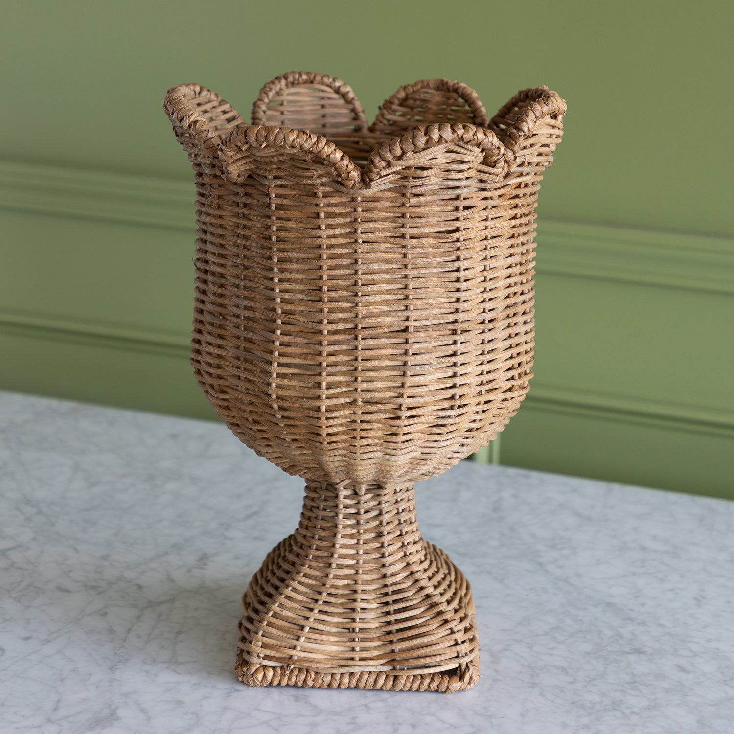 Woven scalloped urn on a marble table with a green background. 