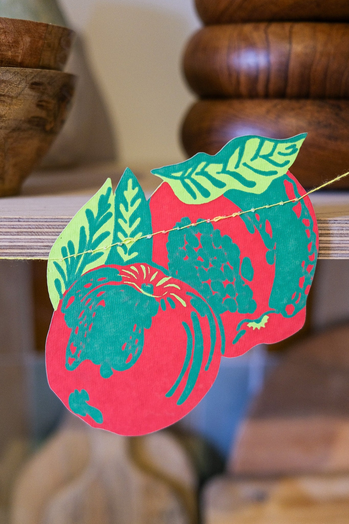 Decorative paper cutout with green leaves and red background, hanging on a wooden surface.