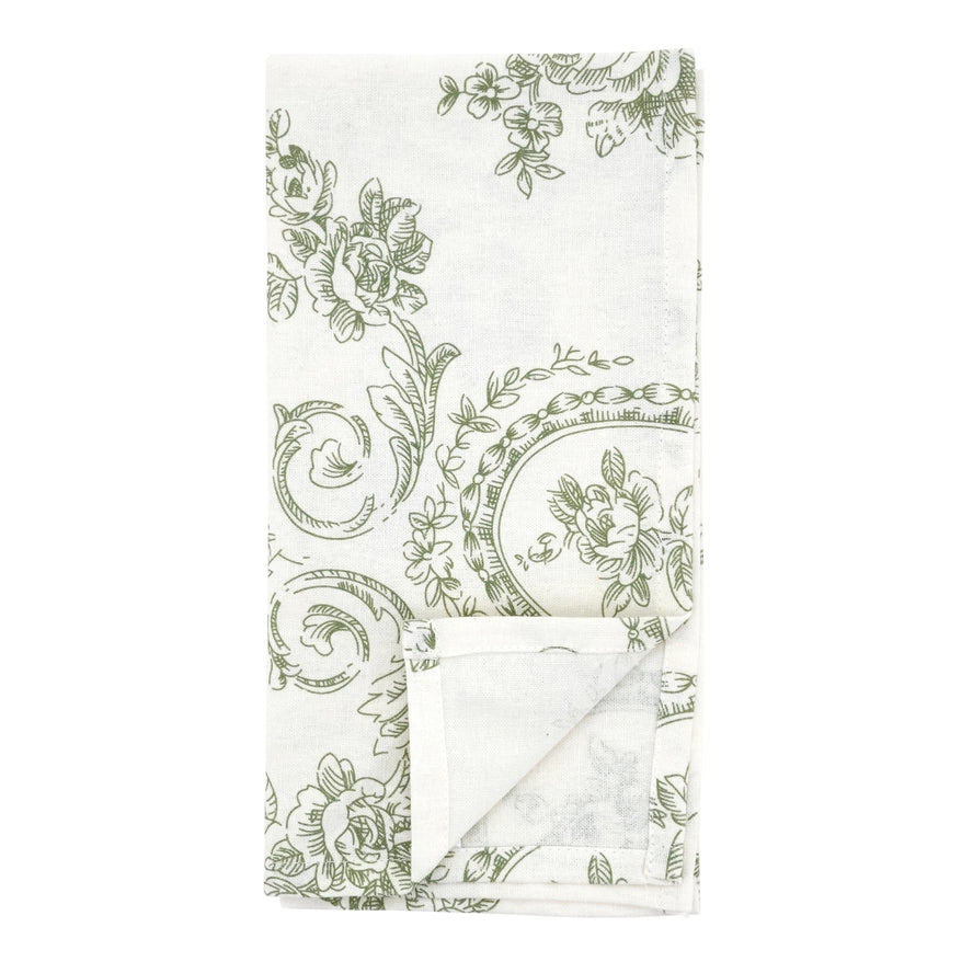 A folded white fabric napkin featuring a classic green toile floral and scroll pattern, with a folded corner showing the plain white reverse side.