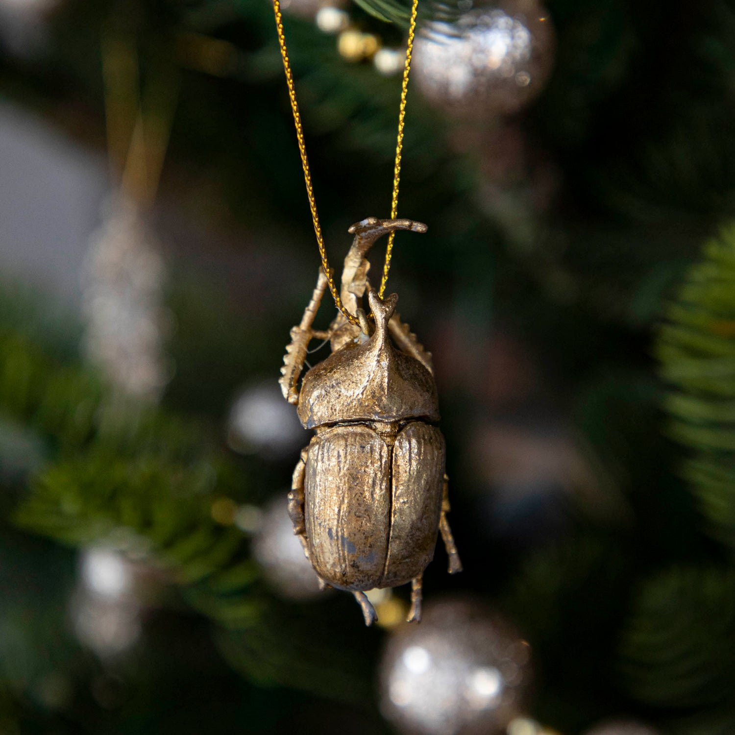 Gold-colored metal beetle-shaped ornament hanging on a Christmas tree.