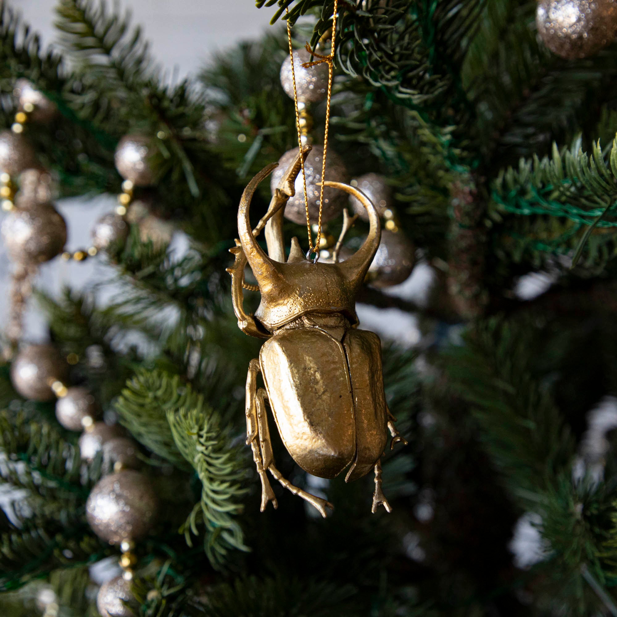 Gold-colored metal beetle-shaped ornament hanging on a Christmas tree.
