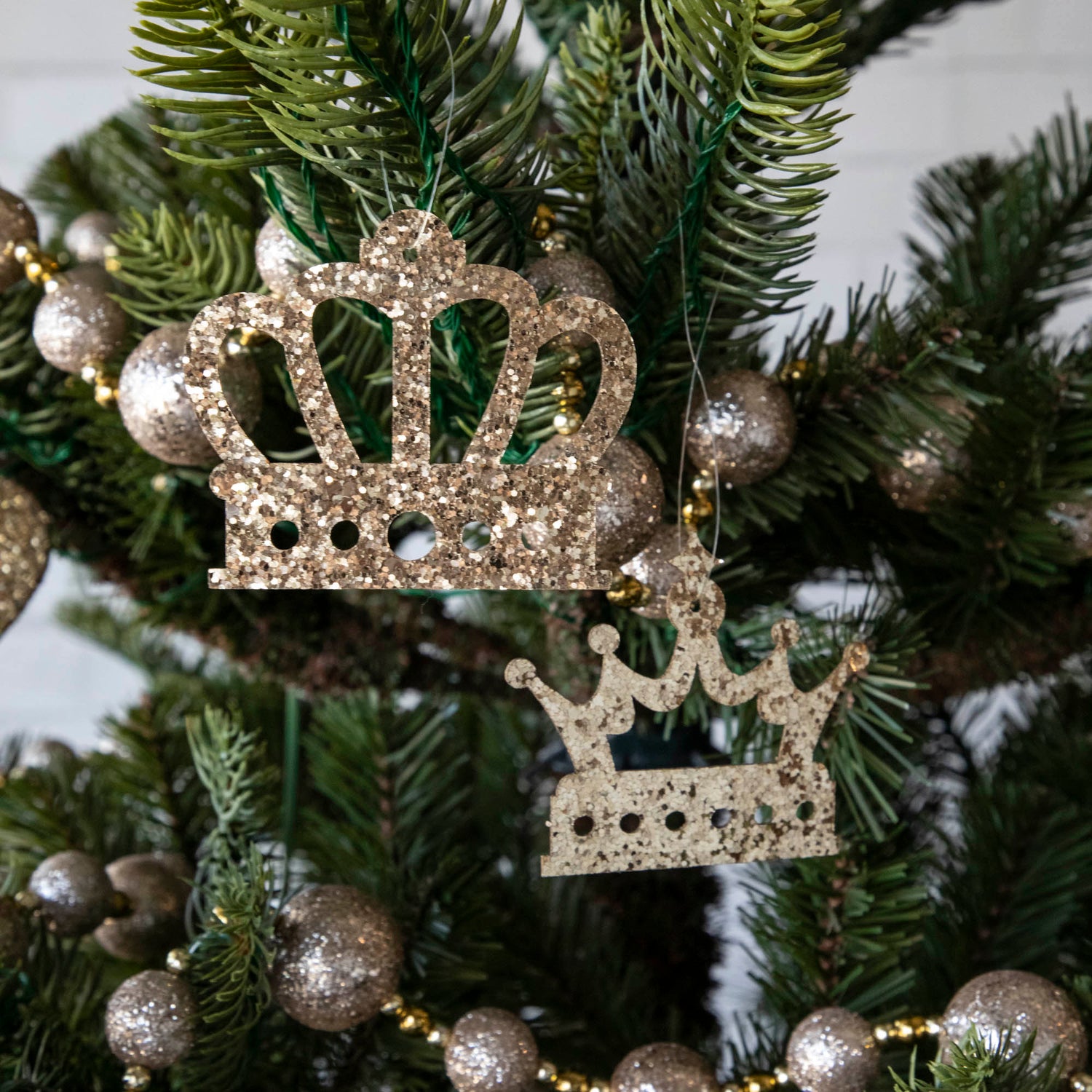 Gold glitter crown-shaped ornaments hanging on a Christmas tree.